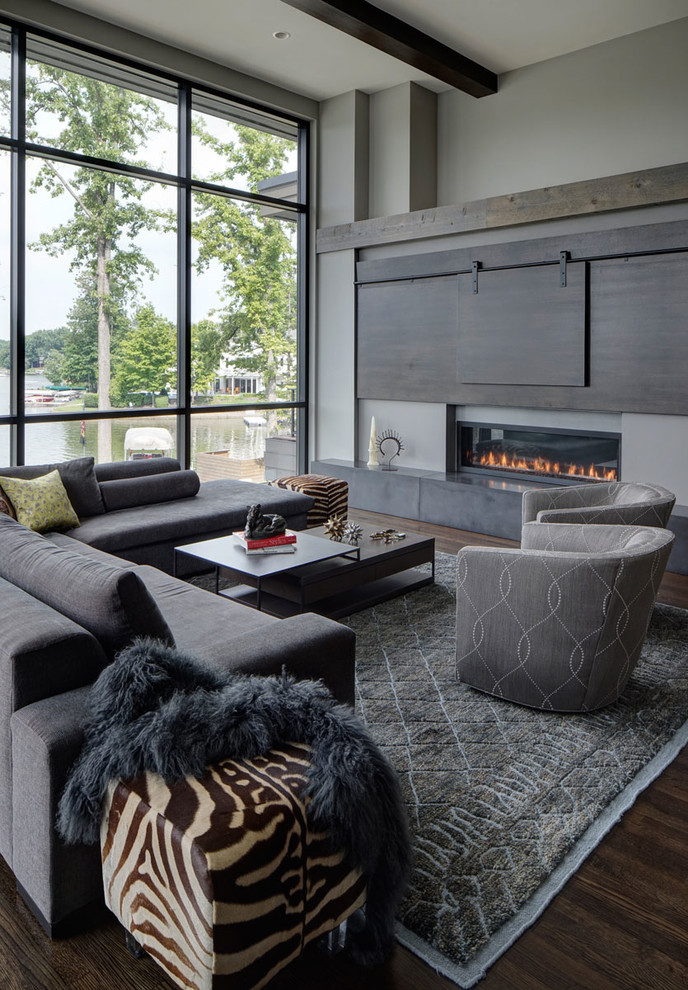 Imagen de sala de estar contemporánea con paredes grises, suelo de madera oscura, televisor retractable, chimenea lineal y alfombra