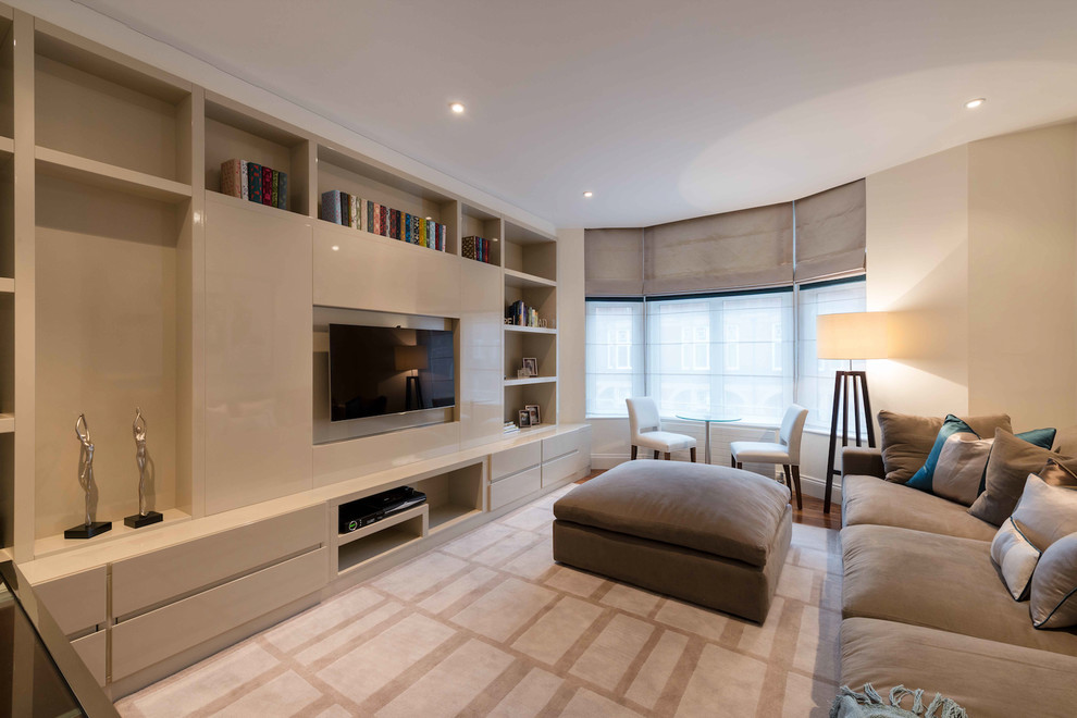 Imagen de sala de estar cerrada actual de tamaño medio sin chimenea con paredes beige, suelo de madera en tonos medios, televisor colgado en la pared y suelo marrón