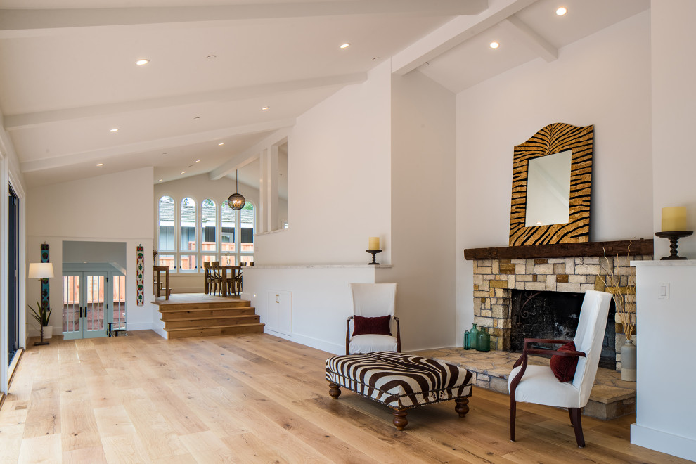 This is an example of a large classic open plan games room in Other with white walls, medium hardwood flooring, a standard fireplace, a stone fireplace surround, brown floors and a vaulted ceiling.