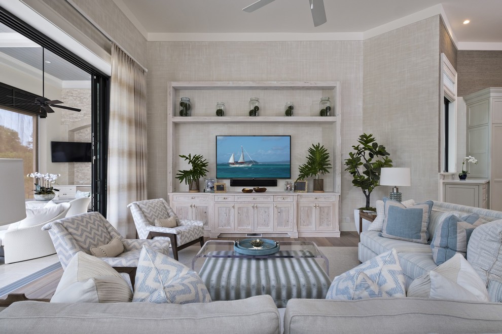 Diseño de sala de estar costera con paredes grises, suelo de madera clara, pared multimedia, suelo beige y alfombra