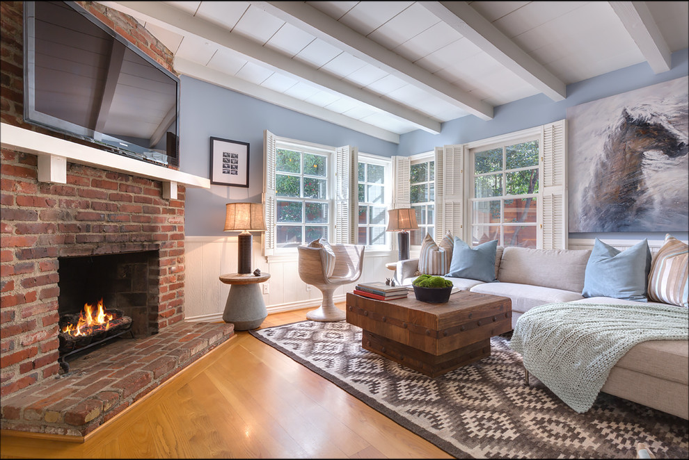 На фото: гостиная комната в морском стиле с синими стенами, паркетным полом среднего тона, стандартным камином, фасадом камина из кирпича и телевизором на стене с