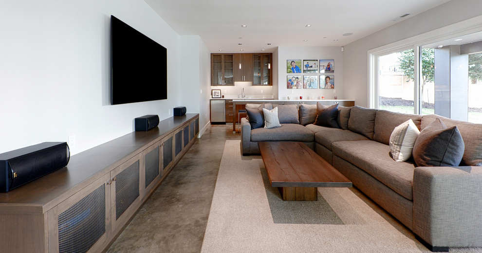 Imagen de sala de estar con barra de bar cerrada actual grande sin chimenea con paredes blancas, suelo de cemento, televisor colgado en la pared y alfombra