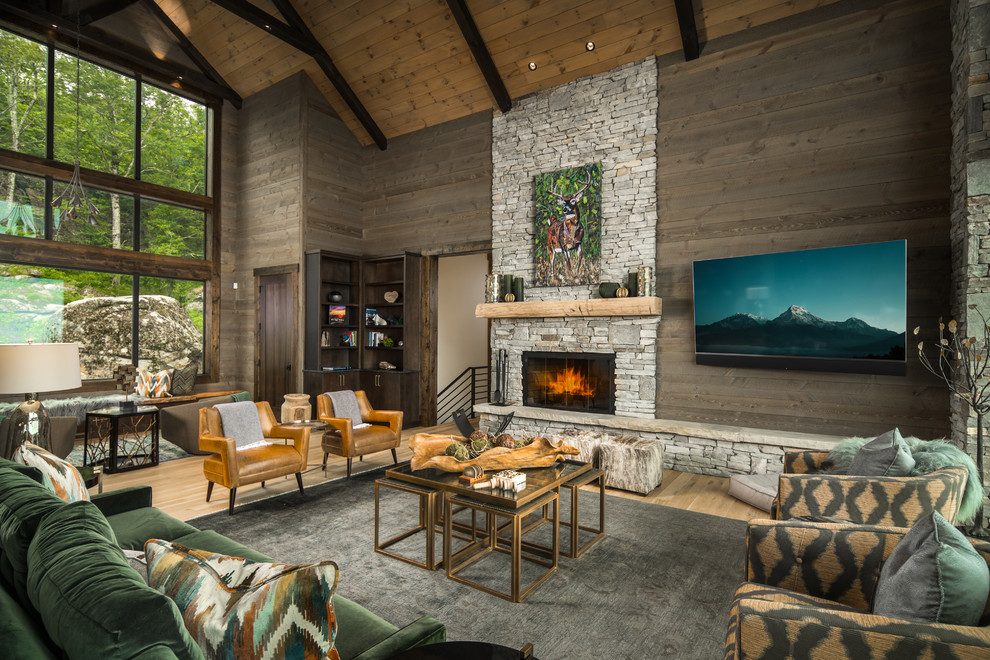 Diseño de sala de estar rural con paredes marrones, suelo de madera clara, chimenea lineal, marco de chimenea de piedra y televisor colgado en la pared