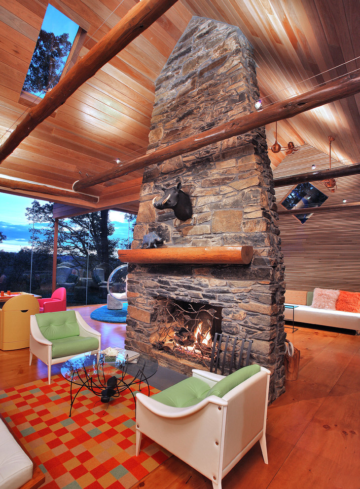 Idées déco pour une salle de séjour éclectique ouverte avec un sol en bois brun, une cheminée standard, un manteau de cheminée en pierre et un sol orange.