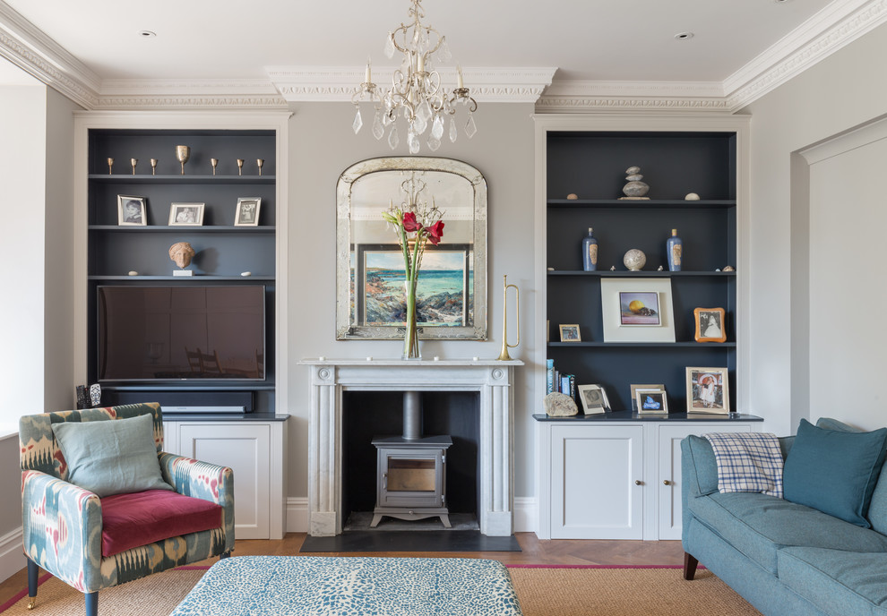 Example of a mid-sized classic medium tone wood floor family room design in London with gray walls, a wood stove and a media wall