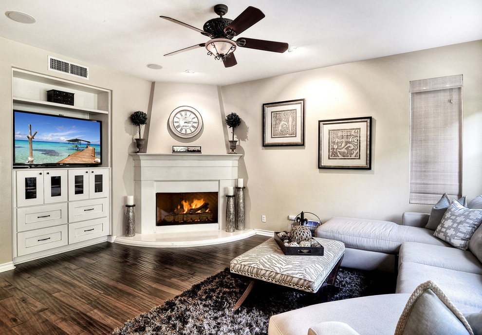 Foto de sala de estar actual grande con paredes beige, suelo de madera en tonos medios, chimenea de esquina, marco de chimenea de yeso, televisor colgado en la pared y suelo marrón