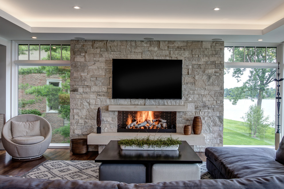 Inspiration for a medium sized traditional enclosed games room in Detroit with white walls, dark hardwood flooring, a standard fireplace, a stone fireplace surround, a wall mounted tv and brown floors.