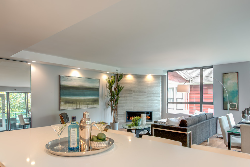 Mittelgroßes, Fernseherloses, Offenes Wohnzimmer mit blauer Wandfarbe, braunem Holzboden, Eckkamin und gefliester Kaminumrandung in Vancouver