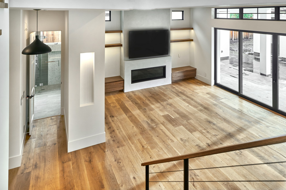 Imagen de sala de estar abierta moderna de tamaño medio con paredes blancas, suelo de madera clara, chimenea lineal, marco de chimenea de yeso, televisor colgado en la pared y suelo marrón
