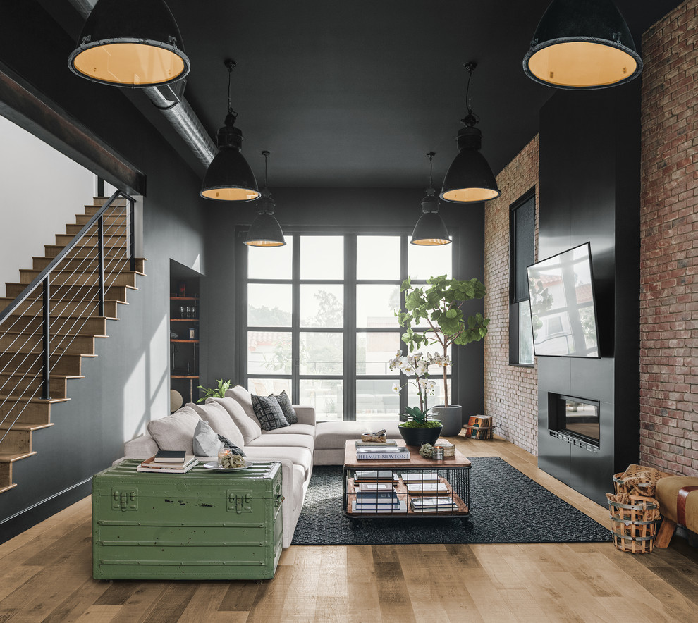 Источник вдохновения для домашнего уюта: открытая гостиная комната в стиле лофт с черными стенами, светлым паркетным полом, горизонтальным камином, телевизором на стене и ковром на полу