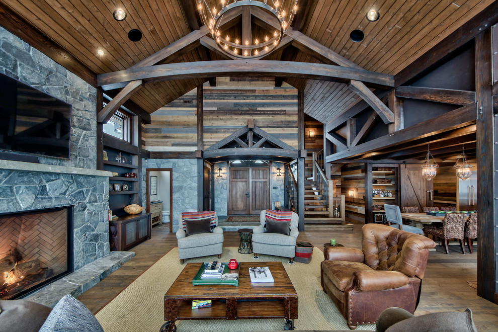 Modelo de sala de estar abierta rural grande con suelo de madera en tonos medios, todas las chimeneas, marco de chimenea de piedra y televisor colgado en la pared