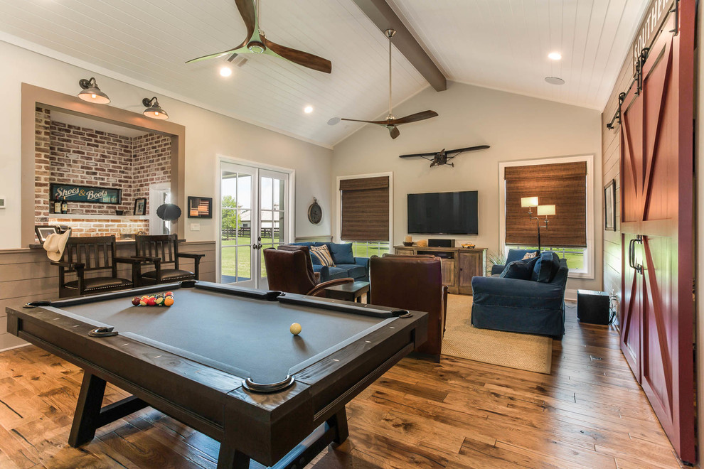 Farmhouse open plan games room in Houston with a game room, medium hardwood flooring, a wall mounted tv and brown floors.