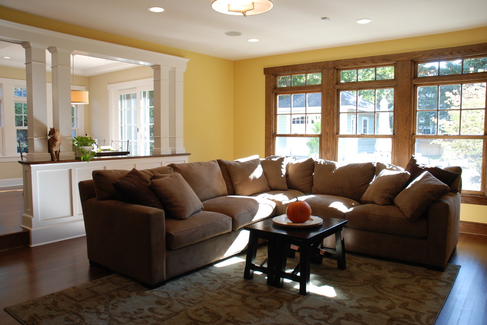 Ejemplo de sala de estar abierta de estilo americano grande con paredes amarillas y suelo de madera oscura