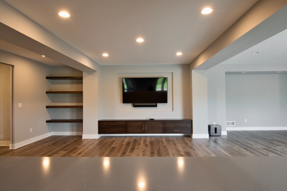 Imagen de sala de estar abierta moderna grande con paredes grises, suelo vinílico, televisor colgado en la pared, suelo marrón y bandeja