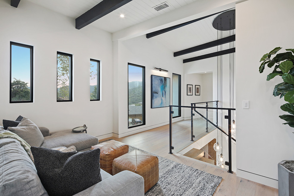 This is an example of a medium sized modern open plan games room in Los Angeles with white walls, light hardwood flooring, no fireplace, no tv, beige floors, exposed beams and a vaulted ceiling.