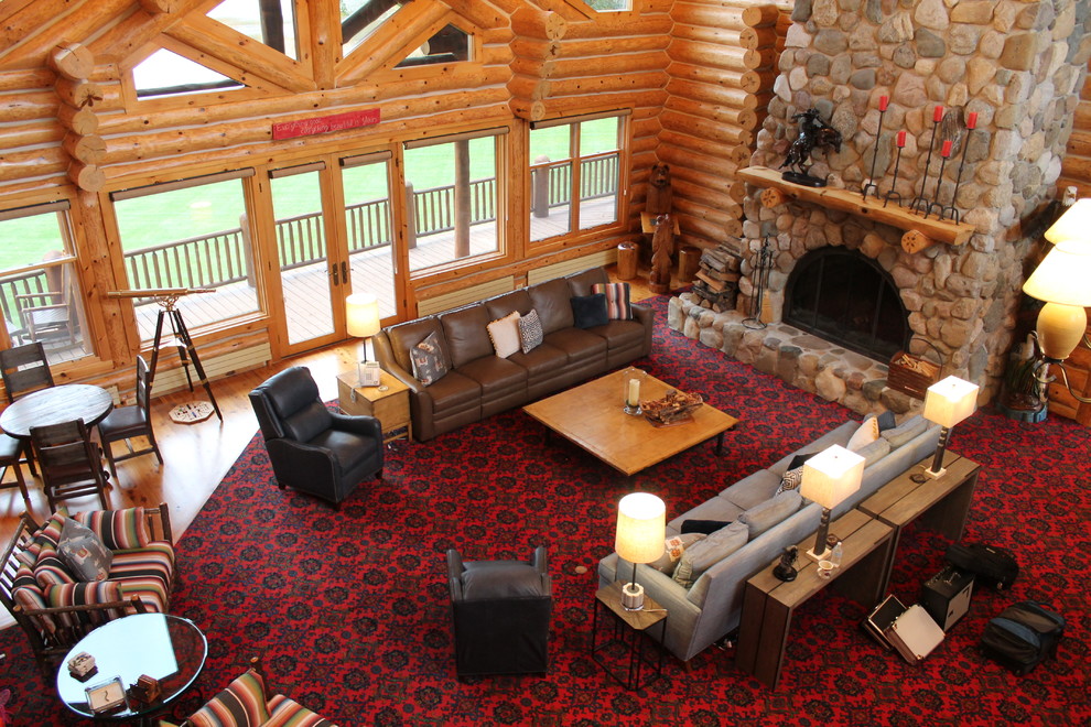 This is an example of a large rustic games room in Grand Rapids with carpet, a standard fireplace, a stone fireplace surround and red floors.