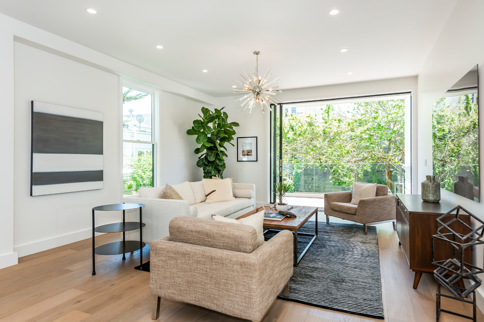 Diseño de sala de estar abierta actual de tamaño medio sin chimenea con paredes blancas, suelo de madera clara, televisor colgado en la pared y suelo marrón