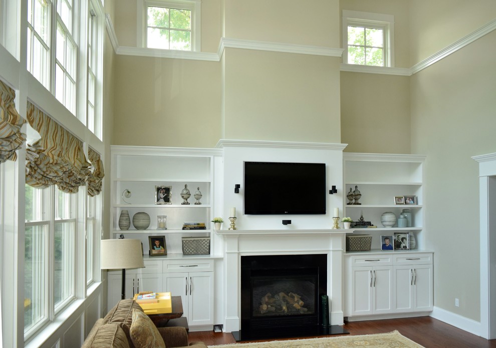 Example of a large classic open concept medium tone wood floor and brown floor family room design in Philadelphia with beige walls, a standard fireplace, a wood fireplace surround and a wall-mounted tv