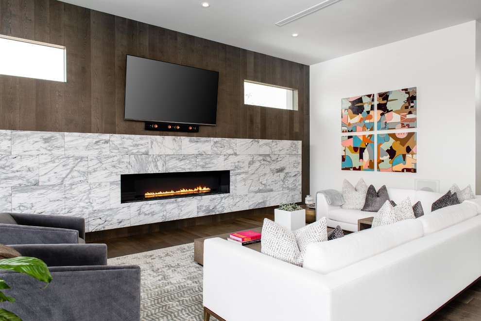 Ejemplo de sala de estar abierta contemporánea de tamaño medio con chimenea lineal, televisor colgado en la pared, paredes blancas, suelo de madera oscura y marco de chimenea de piedra