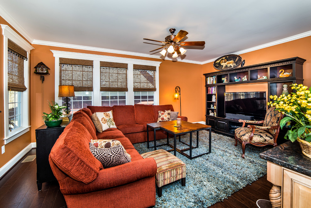 Modelo de sala de estar cerrada clásica renovada grande sin chimenea con parades naranjas, suelo de madera oscura, televisor independiente y suelo marrón