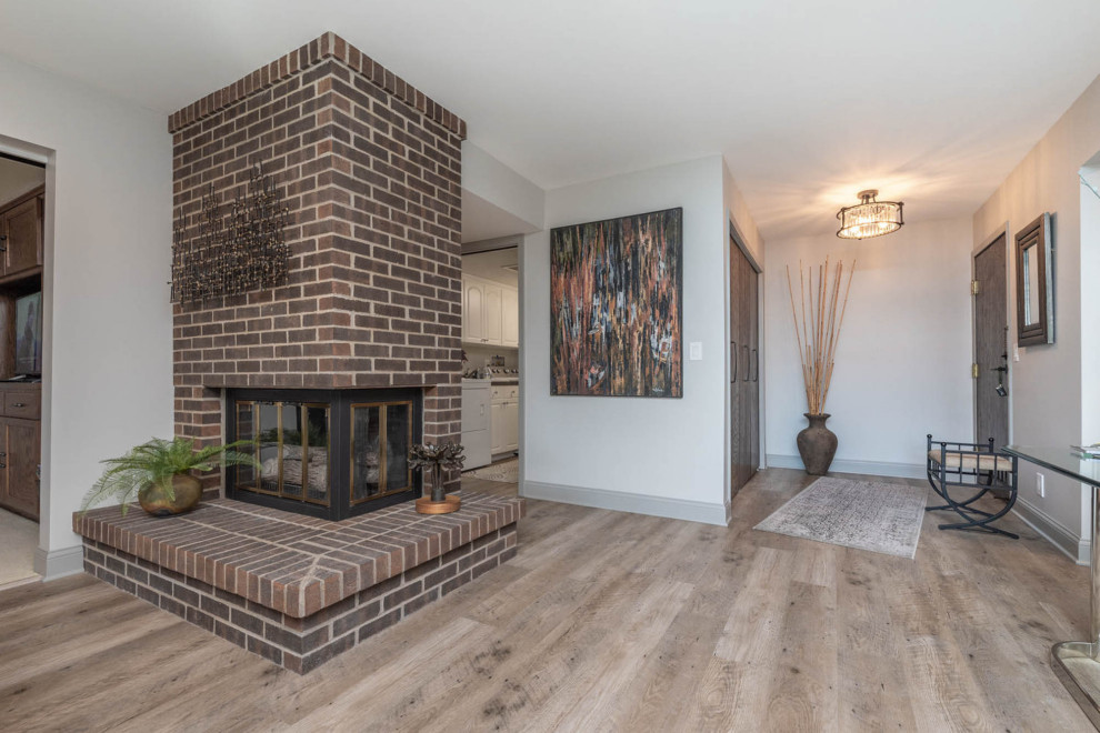 Modelo de sala de estar abierta bohemia de tamaño medio con paredes grises, suelo de madera clara, chimenea de doble cara, marco de chimenea de ladrillo, televisor colgado en la pared y suelo marrón