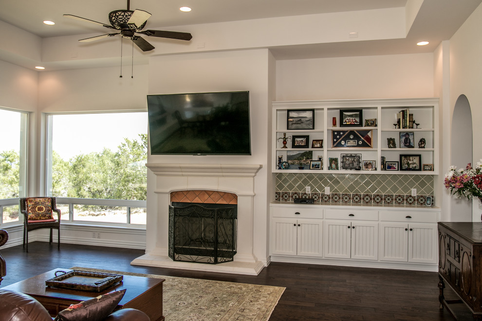 Design ideas for a medium sized mediterranean enclosed games room in Austin with white walls, dark hardwood flooring, a standard fireplace, a tiled fireplace surround, a wall mounted tv and brown floors.