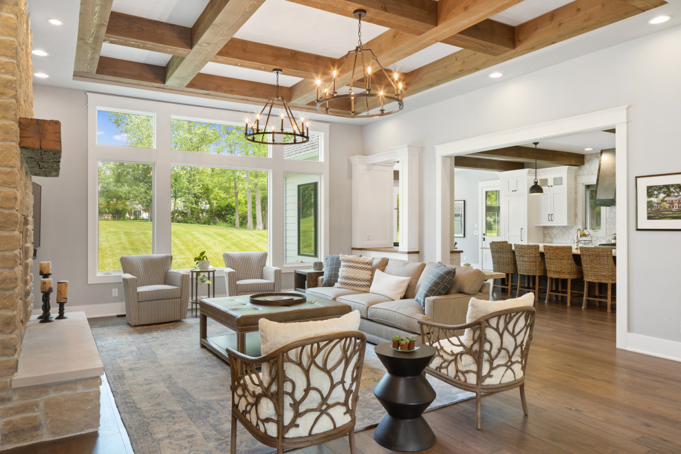 Modelo de sala de estar de estilo de casa de campo grande con suelo de madera en tonos medios, marco de chimenea de piedra y vigas vistas