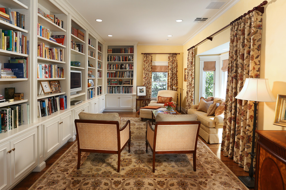 Modelo de sala de estar con biblioteca cerrada tradicional de tamaño medio con paredes amarillas, suelo de madera oscura y televisor independiente