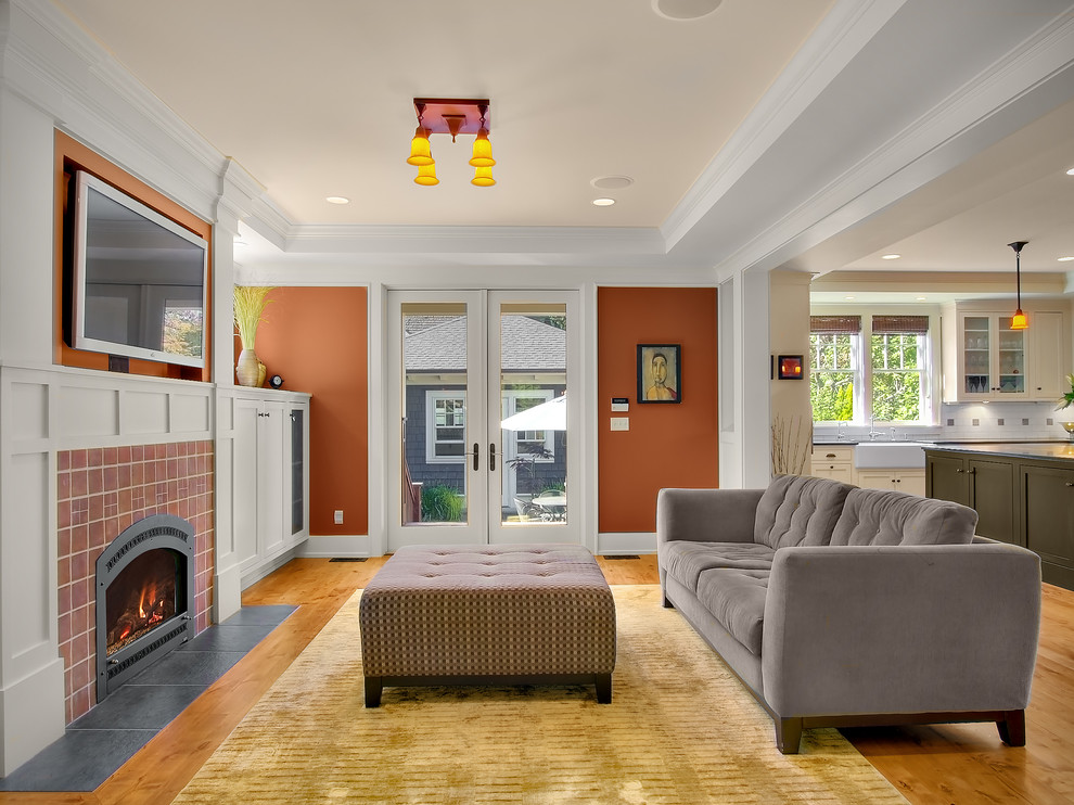 Idée de décoration pour une salle de séjour craftsman de taille moyenne et ouverte avec un mur orange, parquet clair, une cheminée standard, un manteau de cheminée en carrelage et un téléviseur fixé au mur.