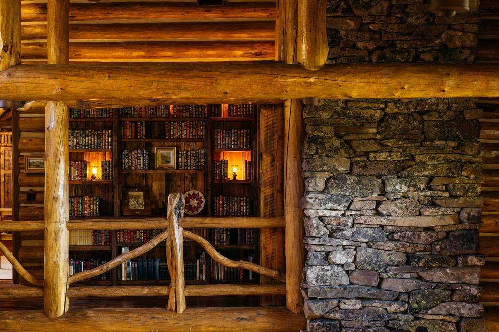 Cette photo montre une grande salle de séjour montagne ouverte avec une bibliothèque ou un coin lecture, un sol en bois brun, une cheminée standard et un manteau de cheminée en pierre.