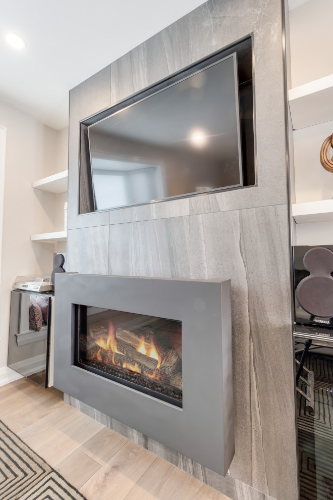 Cette photo montre une salle de séjour tendance de taille moyenne et ouverte avec un mur gris, un sol en bois brun, cheminée suspendue, un manteau de cheminée en carrelage, un téléviseur encastré et un sol marron.