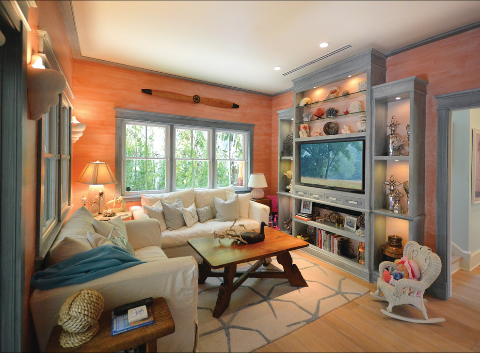 Modelo de sala de juegos en casa cerrada costera de tamaño medio sin chimenea con paredes rosas, suelo de madera clara y pared multimedia