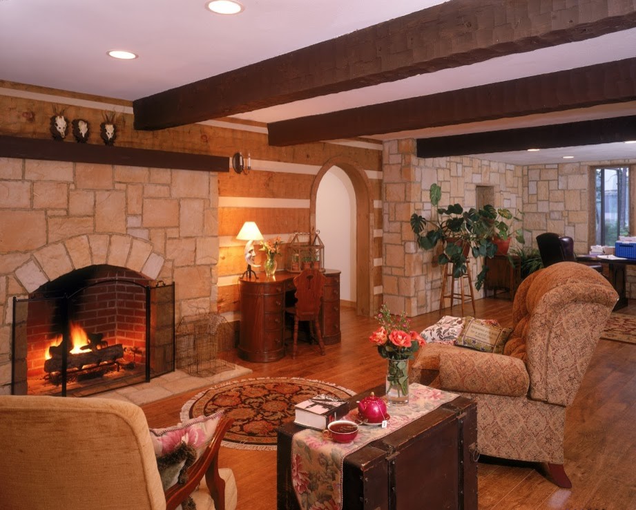Imagen de sala de estar cerrada rural de tamaño medio con suelo de madera en tonos medios, todas las chimeneas y marco de chimenea de piedra