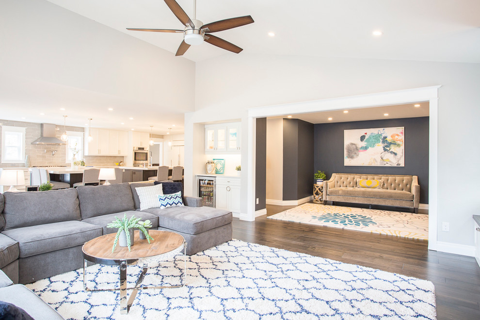 Diseño de sala de estar abierta clásica renovada grande con paredes grises, suelo de madera en tonos medios, televisor colgado en la pared y suelo marrón