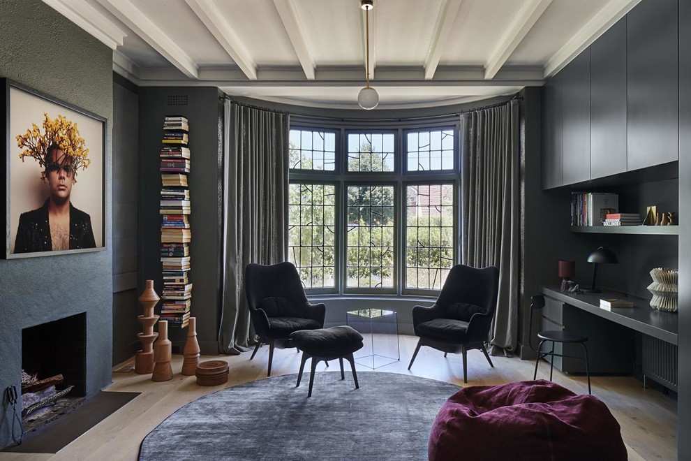 Ejemplo de despacho actual con biblioteca, paredes negras, suelo de madera clara y todas las chimeneas