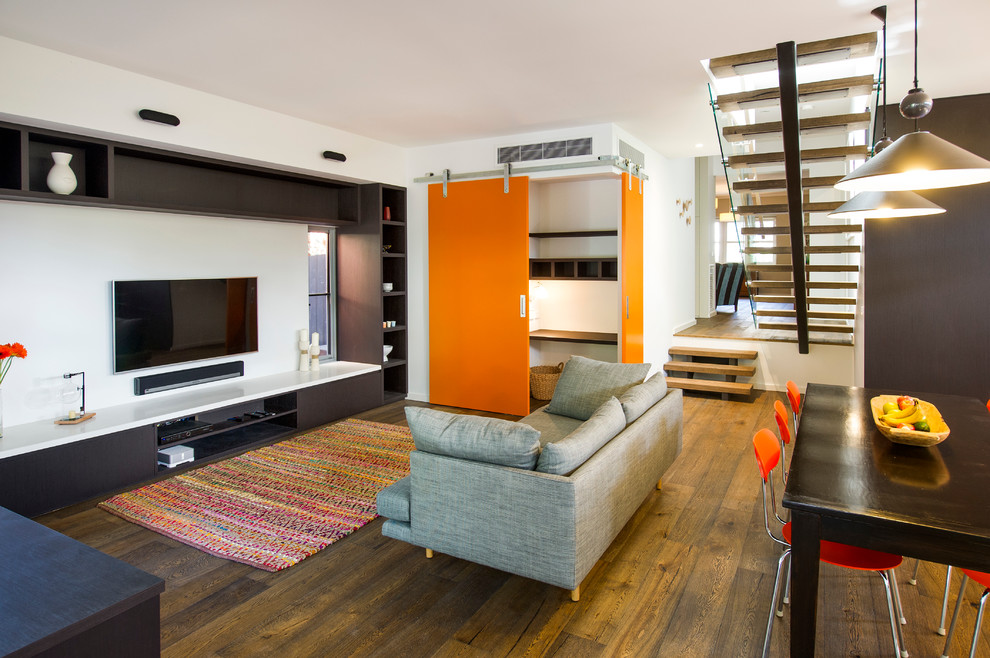 Imagen de sala de estar abierta contemporánea sin chimenea con paredes blancas, suelo de madera en tonos medios y televisor colgado en la pared