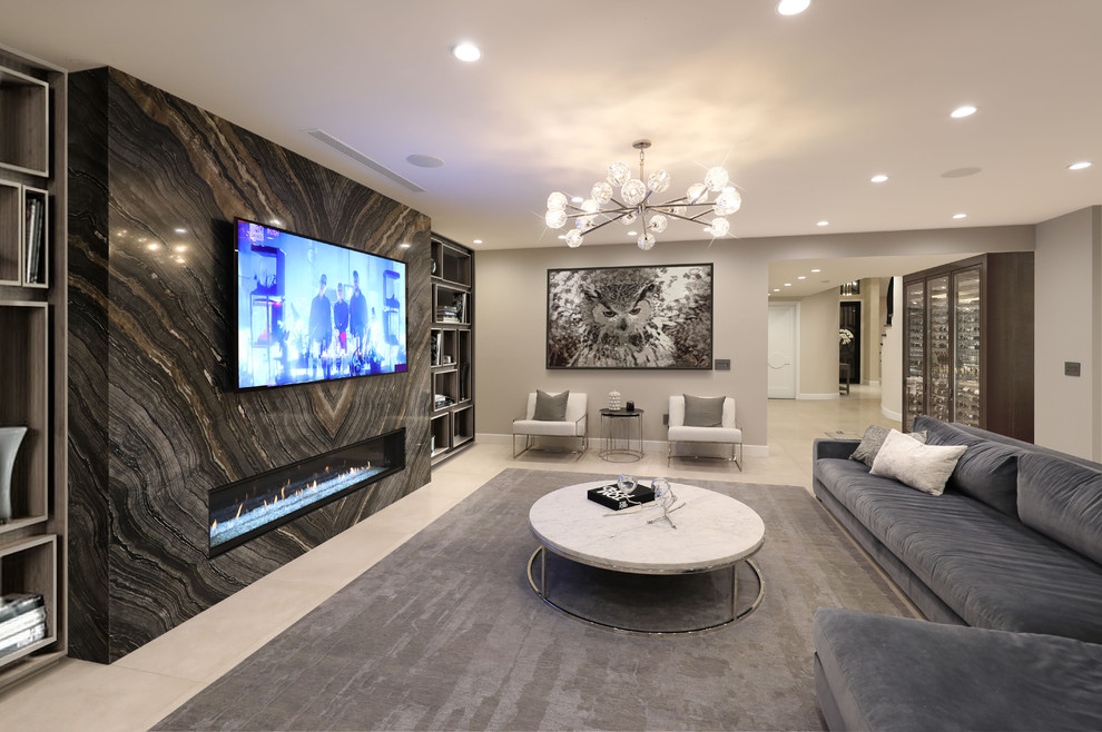 На фото: большая открытая гостиная комната в современном стиле с домашним баром, бежевыми стенами, полом из керамогранита, стандартным камином, фасадом камина из камня, телевизором на стене и серым полом с