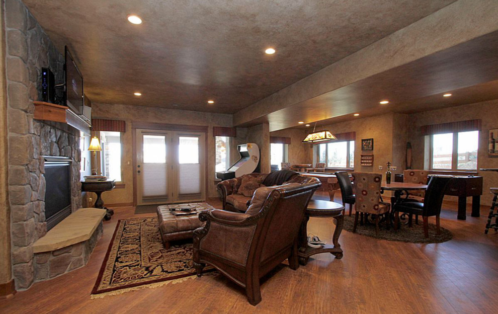 Large mountain style open concept laminate floor game room photo in Denver with brown walls, a standard fireplace, a stone fireplace and a wall-mounted tv