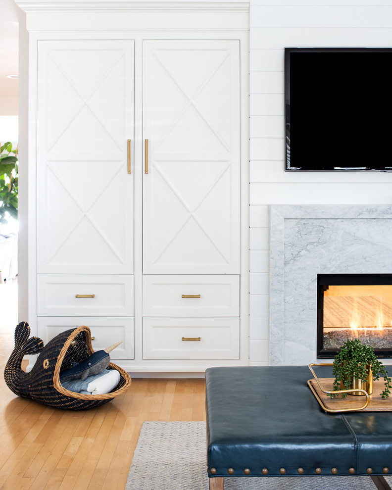 Ejemplo de sala de estar abierta y abovedada costera de tamaño medio con paredes blancas, suelo de madera clara, chimenea de doble cara, marco de chimenea de piedra, televisor colgado en la pared, suelo naranja y panelado