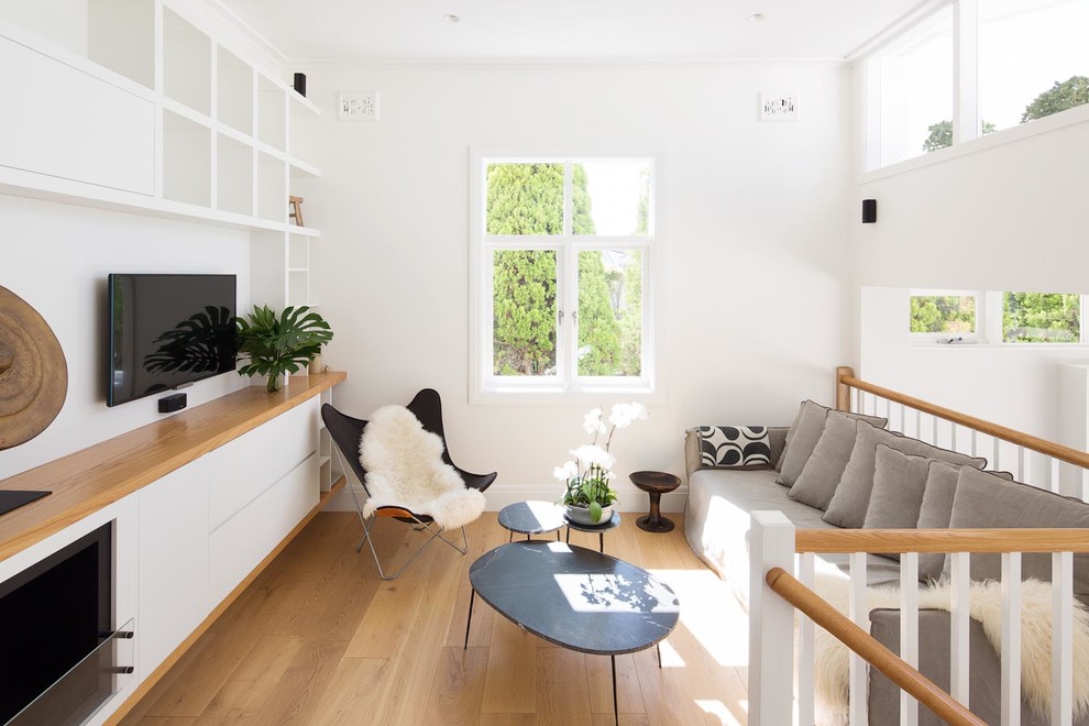 Diseño de sala de estar tipo loft costera con paredes blancas, suelo de madera en tonos medios, televisor colgado en la pared y suelo beige