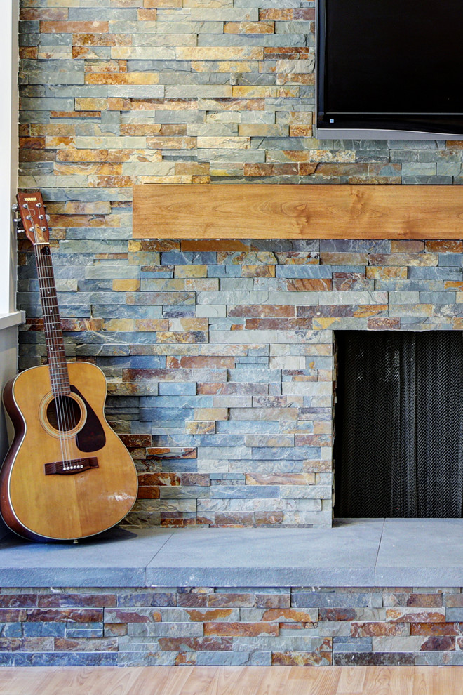 Идея дизайна: большая открытая гостиная комната в стиле неоклассика (современная классика) с серыми стенами, полом из ламината, стандартным камином, фасадом камина из камня и телевизором на стене