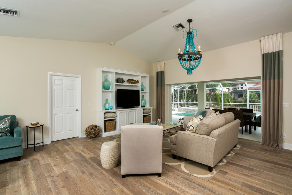 Foto de sala de estar abierta costera con paredes beige, suelo de madera en tonos medios y pared multimedia