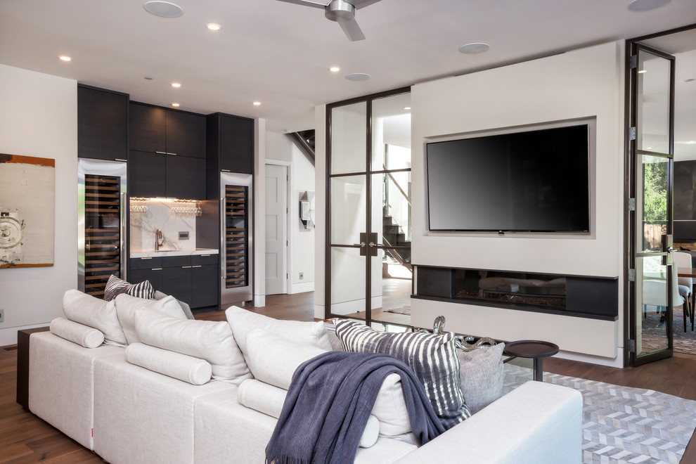Стильный дизайн: открытая гостиная комната в современном стиле с белыми стенами, темным паркетным полом, горизонтальным камином, фасадом камина из металла и телевизором на стене - последний тренд
