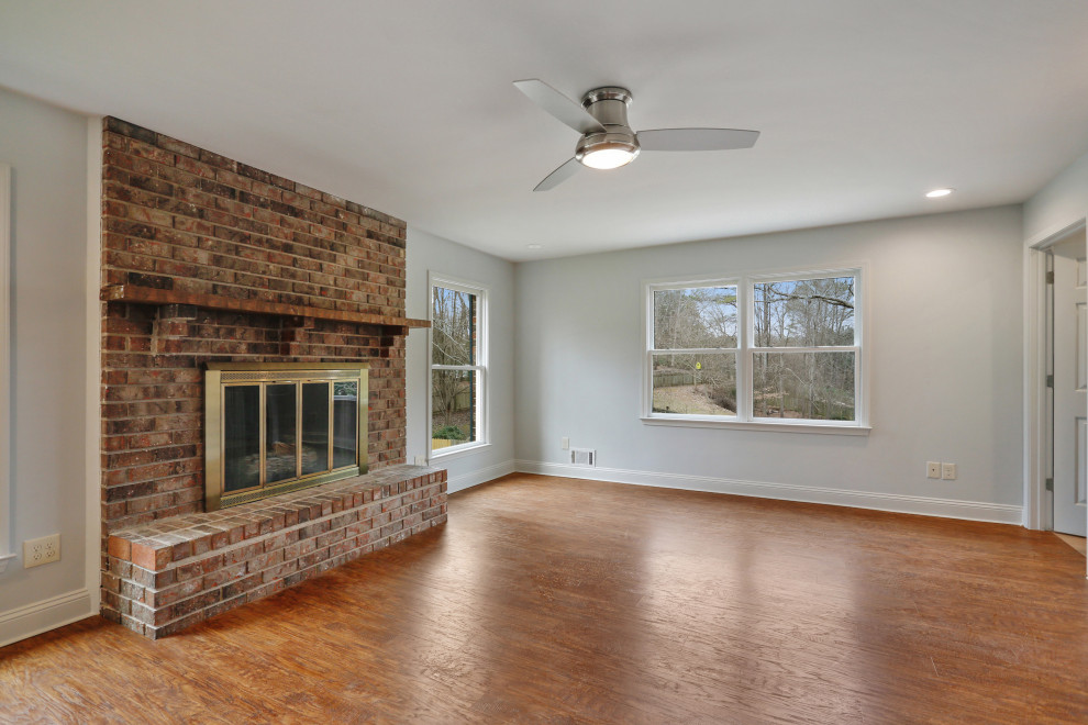 Inspiration for a large contemporary open plan games room in Atlanta with white walls, light hardwood flooring, a standard fireplace, a brick fireplace surround, a wall mounted tv and brown floors.