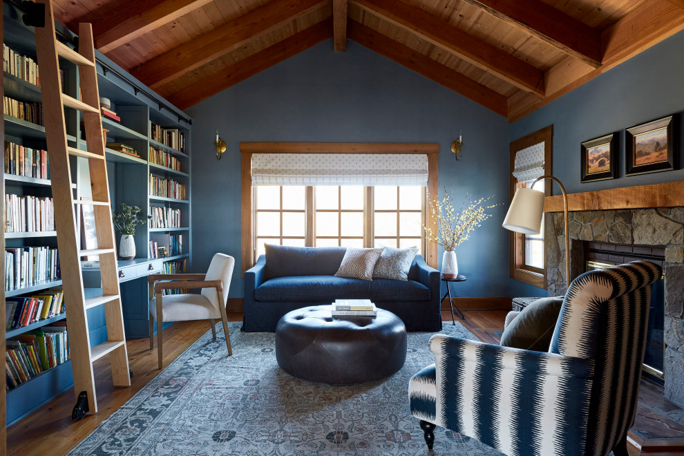 Foto de sala de estar con biblioteca abovedada rural con paredes azules, suelo de madera en tonos medios, todas las chimeneas, marco de chimenea de piedra, suelo marrón, vigas vistas y madera