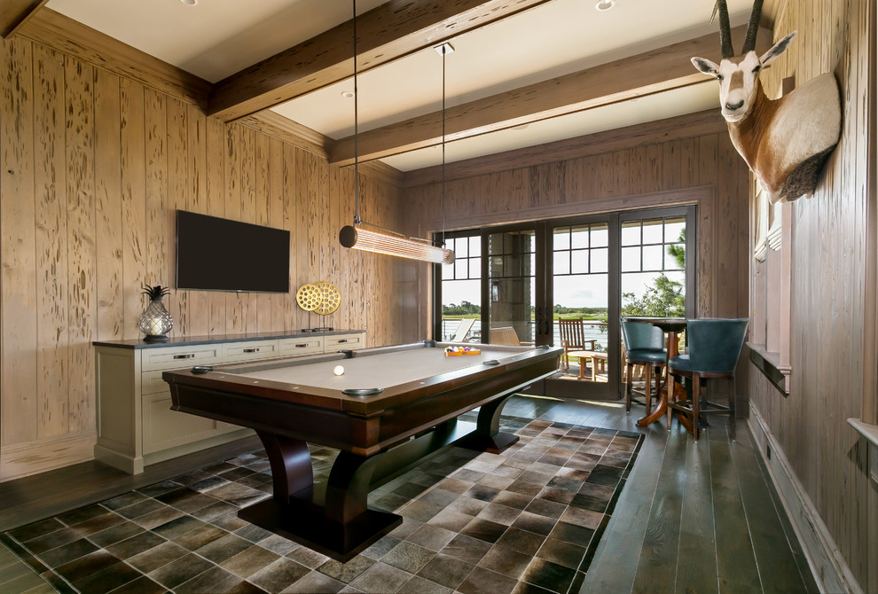 Modelo de sala de juegos en casa costera grande con paredes beige, suelo de madera oscura, televisor colgado en la pared y suelo marrón