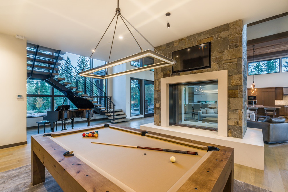 Large contemporary open plan games room in Sacramento with white walls, light hardwood flooring, a two-sided fireplace, a concrete fireplace surround, a wall mounted tv and brown floors.
