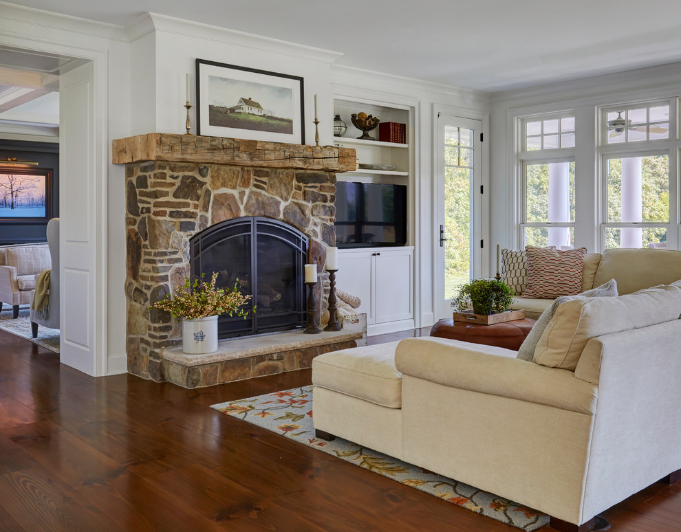 This is an example of a large country open plan games room in Chicago with white walls, dark hardwood flooring, a standard fireplace, a stone fireplace surround, a built-in media unit and brown floors.