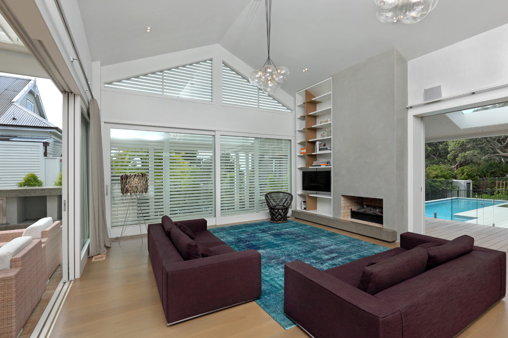 Imagen de sala de estar abierta actual con paredes blancas, suelo de madera clara, todas las chimeneas, televisor independiente y alfombra
