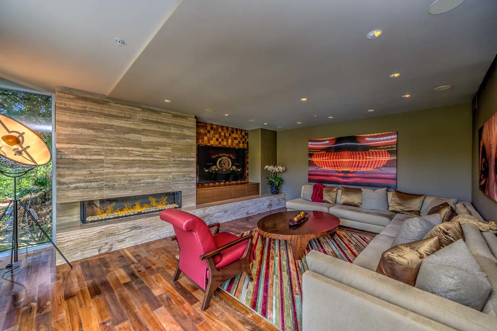 Large contemporary open plan games room in Los Angeles with green walls, medium hardwood flooring, a built-in media unit, a corner fireplace, a tiled fireplace surround and brown floors.